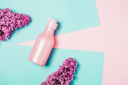 Creative minimal beauty and health background with pink bottle and lilac flowers. Minimal top view and flat lay of cosmetic on pink and blue trendy background.の写真素材