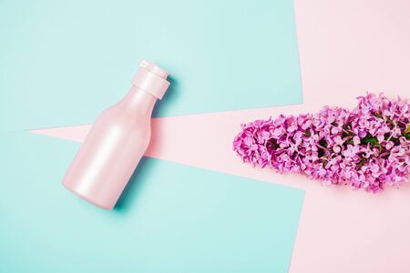 Creative minimal beauty and health background with pink bottle and lilac flowers. Minimal top view and flat lay of cosmetic on pink and blue trendy background.の写真素材