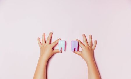 Child's hands holding big tooth and toothbrush on pink backgroubd. Healty care teeth concept. Top view, flat lay. Copy space for your textの写真素材