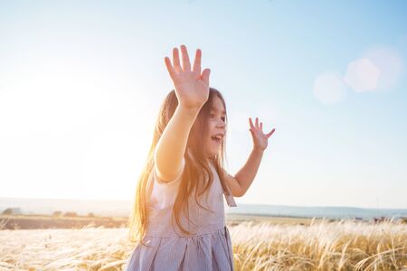Pretty happy little girl in pink dress with long hair walking outdoors in summer field on sunset.の写真素材