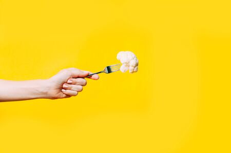 Female hand holding fork and broccoli on it on yellow background. Minimal concept of healthy eating and vegan.の写真素材
