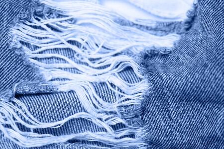 Macro texture of jeans hole and threads colored in classic blue.