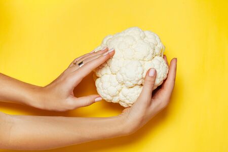Female hand holding broccoli on yellow background. Minimal vegan concept. Healthy eating.の写真素材