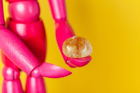 Amber semiprecious piece of stone in hands of pink wooden manikin. Bright and vibrant.