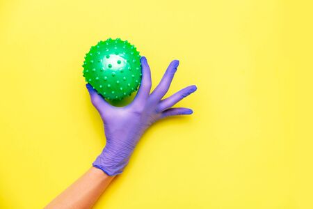 Hand in rubber glove holding coronavirus on yellow background.の写真素材