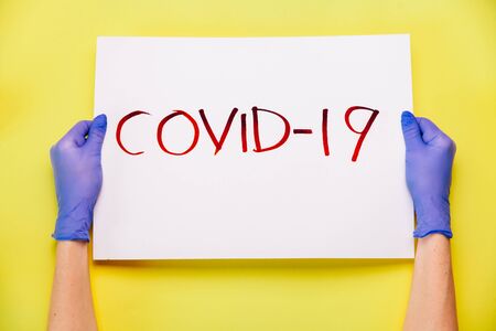 COVID-19 Coronavirus creative concept. Hands in gloves holding poster vith COVID-19 wordの写真素材