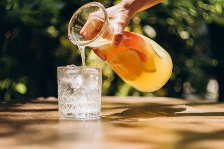 Glass of lemonade with ice on little table in summer yard