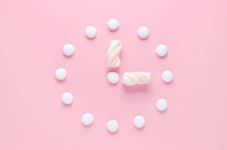 concept image, a clock with candy and marshmallow in pastel colors on pinkの写真素材