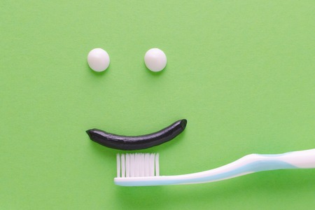 a face with smile from white and black toothpaste, teeth care concept, toothbrush on green backgroundの写真素材