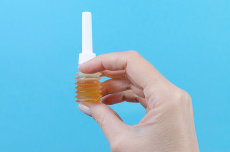 womans hand with mini enema on blue backgroundの写真素材