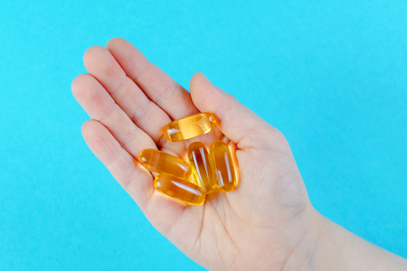childs hand with omega capsules on blue backgroundの写真素材