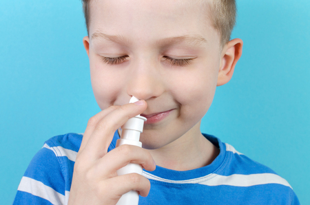 portrait of smiling boy with nasal spray, blue backgroundの写真素材
