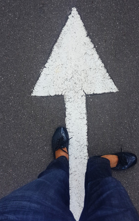 feet on tarmac road with white direction arrowの写真素材