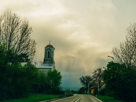 Rainbow in the sky above the church and road.の写真素材