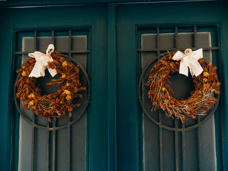 Two brown wreaths with bows on green doors with metal grill.の写真素材