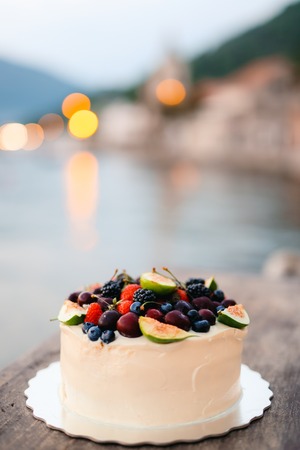 Wedding cake of figs, cherries and berries with a white cream. On the table in a cafe on the beach.の写真素材