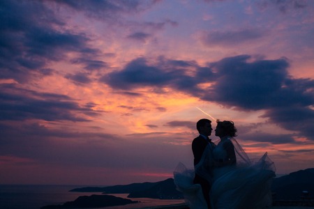 Silhouette of the newlyweds against the sky at sunset. Wedding in Montenegro. Silhouette of a couple. Silhouette of the bride and groom.の写真素材