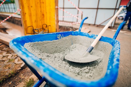Blue clean new wheelbarrow for cement. Laying the first shovel cement in the foundation on the construction of the house.の写真素材