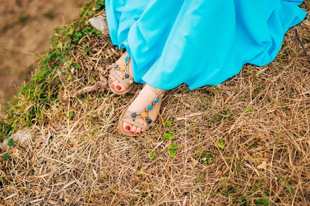 Female feet in sandals. On dry grass. A girl in a blue sarafan.の写真素材