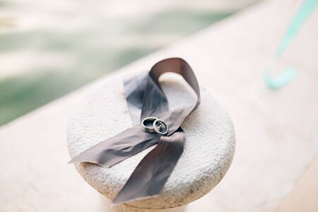 Wedding rings lie on a gray ribbon. On a rock near the water.の写真素材