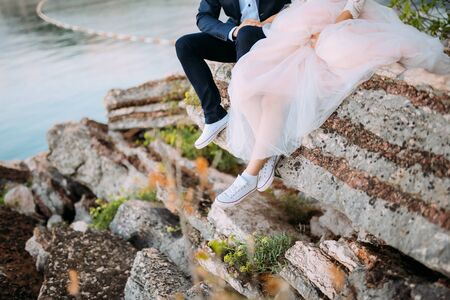 The newlyweds are sitting on the precipice. Legs close-up. Wedding in Montenegro.の写真素材