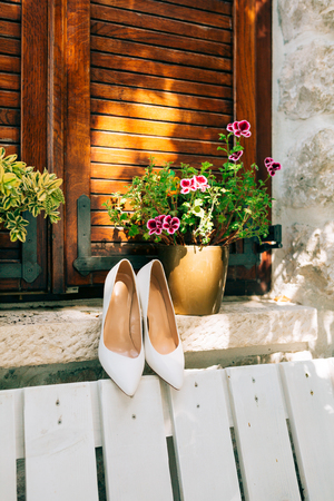 White brides shoes on a white bench and flowers in the background.の写真素材