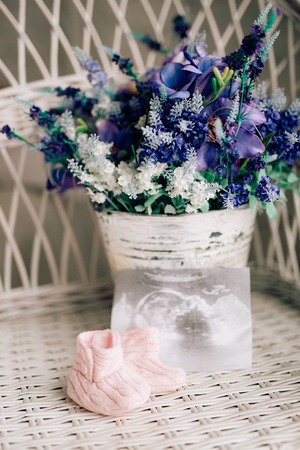 Baby booties on a wicker chair and a bouquet of lavender on a background.