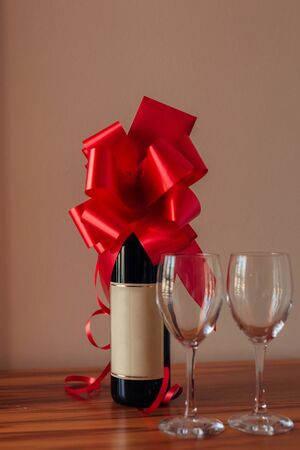 A bottle of champagne on the table and two empty glasses, a bottle tied with a red bow.の写真素材
