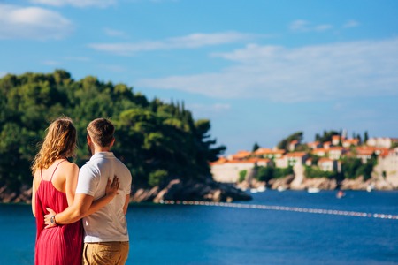 A young couple hugs and looks at the island of Sveti Stefan in Montenegro.の写真素材