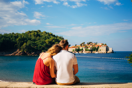 A young couple hugs and looks at the island of Sveti Stefan in Montenegro.の写真素材