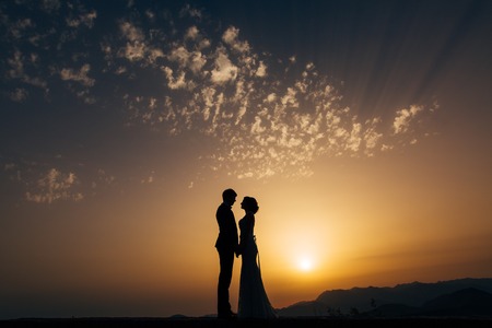 Silhouette of the newlyweds against the sky at sunset. Wedding in Montenegro. Silhouette of a couple. Silhouette of the bride and groom.の写真素材