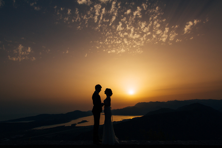 Silhouette of the newlyweds against the sky at sunset. Wedding in Montenegro. Silhouette of a couple. Silhouette of the bride and groom.の写真素材