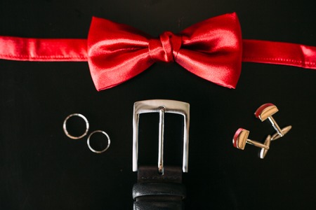 Black shoes of the groom, red bow tie, cufflinks, belt, on a black background with bright bokeh. Wedding groom accessories.の写真素材
