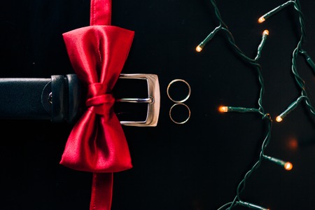Black shoes of the groom, red bow tie, cufflinks, belt, on a black background with bright bokeh. Wedding groom accessories.の写真素材