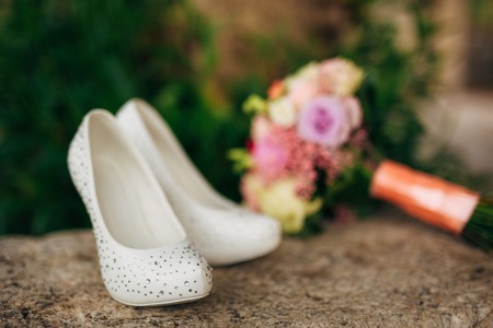 brides shoes lie on the green grass in the forest next to a wedding bouquet of flowers and greeneryの写真素材