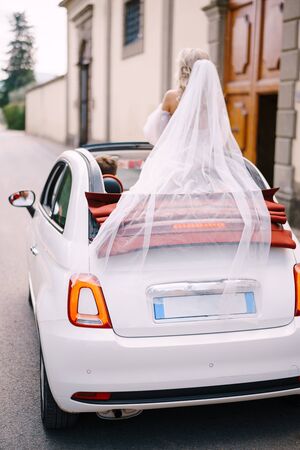 Beautiful bride standing up in a convertible with her back turned to the camera in front of the Medici Villa of Lilliano Wine Estate, Tuscany, Italy.の写真素材
