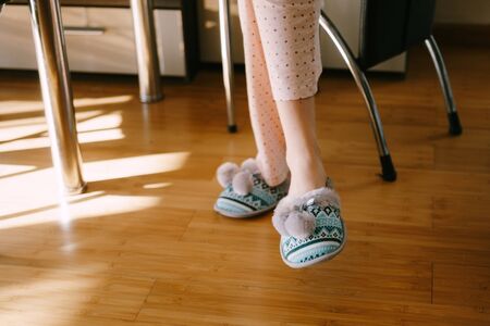 Women's legs in warm home slippers with pattern and bubonic, the girl sits on a chair at table.の写真素材