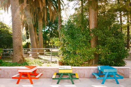 Three tables with benches of different colors. Street furniture in the park. Red, green-yellow and blue tablesの写真素材