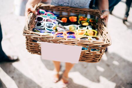 A basket of glasses. A wicker basket of wood with sunglasses of different colors in the hands of a girl.の写真素材