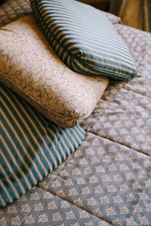 Pillows on the bed. A pillow with a pattern and two pillows with stripes lie on an old wooden bed