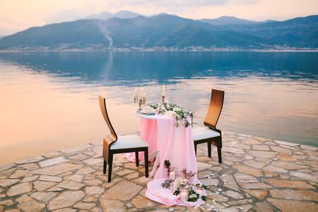 Close-up of a wedding dinner table at reception. Romantic sunset dinner on beach. A table by the sea, at sunset. Dinner for two. Romantic dateの写真素材