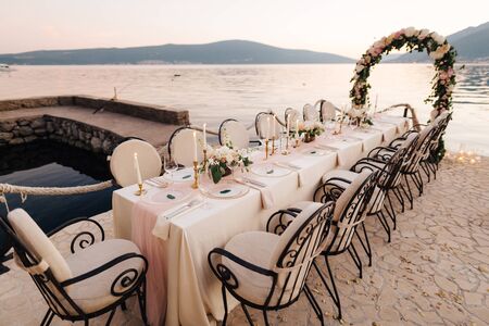 Close-up of a wedding dinner table reception. A table stands on beach overlooking mountains at...