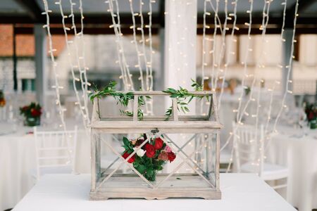 Decoration of the table - a wooden box with glass, with a bouquet of flowers inside of red roses and...