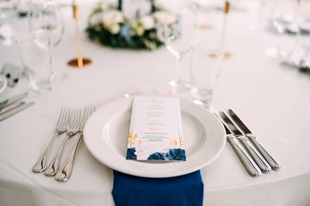 Wedding dinner table reception. White plate on the table, three forks on left, three knives on the...