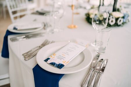 Wedding dinner table reception. White plate on the table, three forks on left, three knives on the...