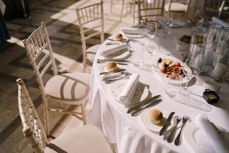 Wedding dinner table reception. Round banquet table with white tablecloth and cream chiseds Chiavari. Dishes are on the table, everyone in the plate is bunの写真素材