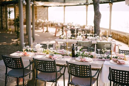 There are many rectangular tables for guests with pink tablecloth, in the rays of sunset on the...