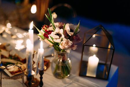 A bouquet of flowers in a glass vase on the table at night. White candles in candlesticks expire with molten waxの写真素材