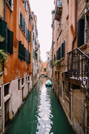 Beautiful narrow canal in Venice, Italy. Between two buildings. A small bridge in distance. Moored...