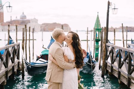 The bride and groom kiss on the gondola pier, hugging, in Venice, near St. Marks Square, overlooking San Giorgio Maggiore and the sunset sky. The largest gondola pier in Venice, Italy.の写真素材